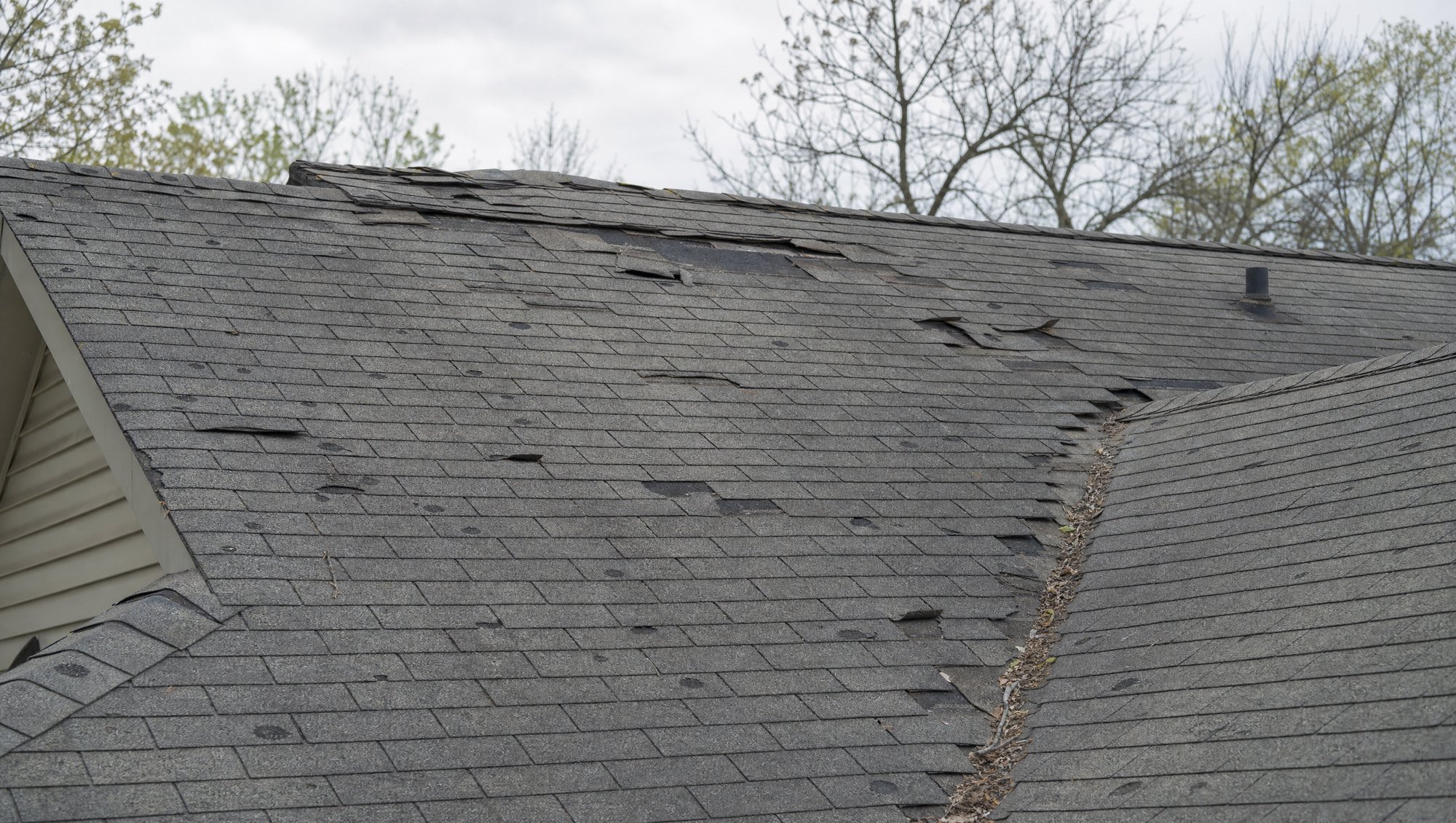 Storm-damaged residential roof with visible hail and wind damage being assessed